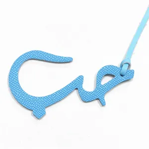 Gros plan d'un charm en cuir bleu clair avec lettre arabe et fine lanière de suspension.