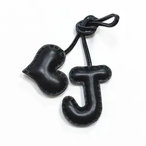 Primo piano dettagliato di un ciondolo per borsa in pelle nera a forma di lettera J e cuore.