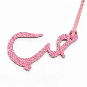 Gros plan du charm de sac en cuir rose représentant une lettre arabe avec texture fine et lanière.