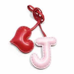 Primo piano dettaglio della lettera J in pelle rosa e ciondolo cuore rosso fatto a mano.