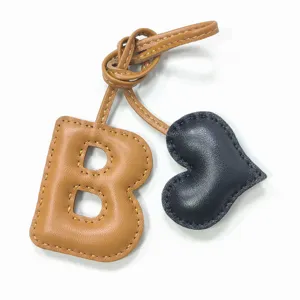 Detalle de dije de bolso letra B de cuero y corazón, accesorio de moda elegante.