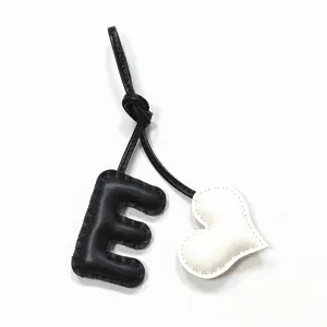 Leather letter E heart bag charm detail, black and white handmade stitching pendant close up.