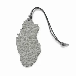 Gros plan du charm de sac en cuir gris en forme de carte du Qatar, avec texture et lanière.