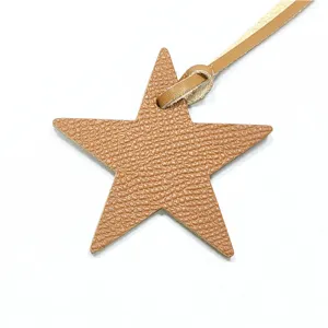 Détail de pendentif étoile en cuir marron, charm de sac texturé avec lanière de suspension.
