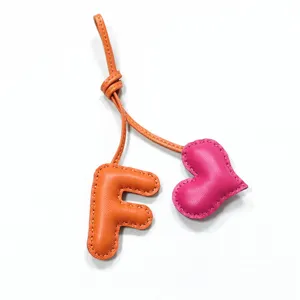 Nahaufnahme von handgefertigtem Leder Buchstaben F und rosa Herz Taschenanhänger mit Naht.