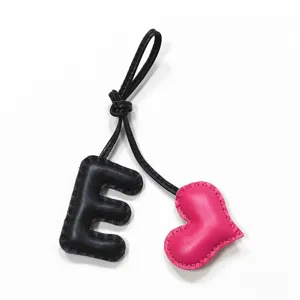 Detailed close-up of a black leather letter E and pink heart charm with leather strap.