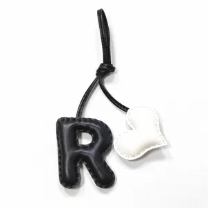 Primo piano dettagliato del ciondolo per borsa con lettera R in pelle nera e cuore.