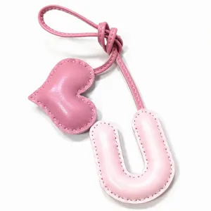 Nahaufnahme des rosafarbenen Leder-Buchstaben U und Herz-Taschenanhängers mit Handnaht.