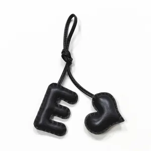 Handmade black leather letter E and heart bag charm detail shot showcasing stitching texture.