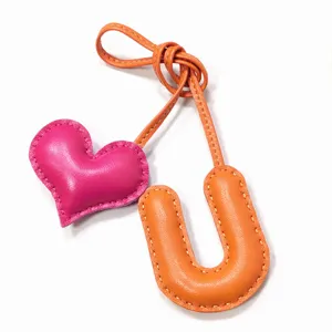 Handgefertigter Leder-Buchstabe U und Herz Taschenanhänger in leuchtendem Orange und Rosa.