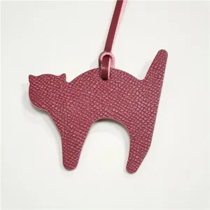 Close-up detail of the burgundy leather cat bag charm pendant, showing fine texture and strap.