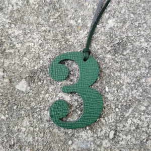 Close-up detail shot of a green textured number three leather bag charm with hanging cord.