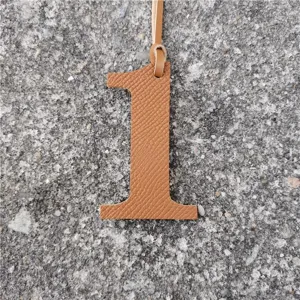 Detailed view of a number 1 leather bag charm in caramel color with textured finish.
