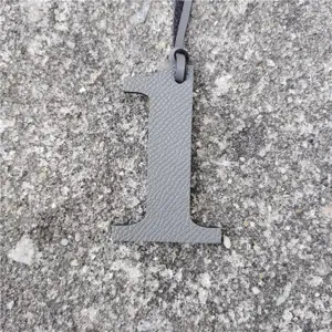 Grey leather number 1 bag charm detail view, minimalist pendant texture close up shot.