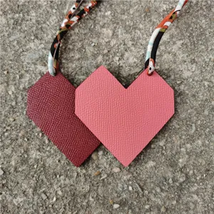 Detailed view of dual-color leather heart and rhombus bag charm with patterned silk strap.