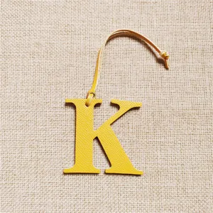 Vue détaillée en gros plan du charm de sac lettre K en cuir jaune avec une sangle.