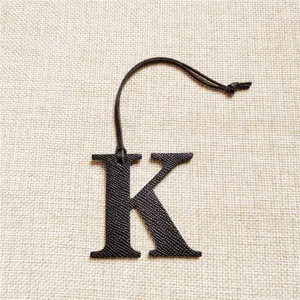 Vue détaillée du pendentif de sac en cuir lettre K noire, présentant une texture et une lanière.