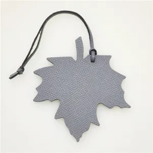 Grey leather maple leaf bag charm and car pendant detail shot, showing textured pendant.