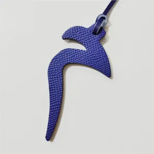 Close-up of blue textured leather Arabic letter bag charm, elegant hanging ornament.