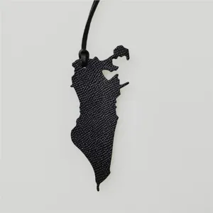 Détail du charm de sac carte en cuir, texture de cuir noir et pendentif forme géographique.