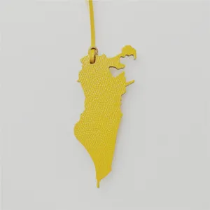 Gros plan du charm de sac en cuir jaune en forme de carte de Bahreïn avec texture fine.