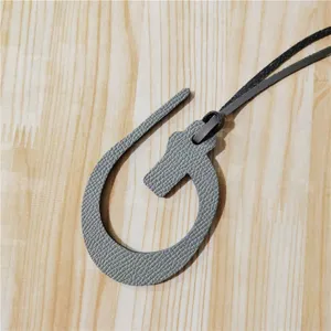 Gros plan détaillé du charm de sac en cuir texturé gris suspendu sur une surface en bois.