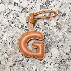 Light brown leather letter G bag charm, stylish initial pendant for women's handbag accessory.