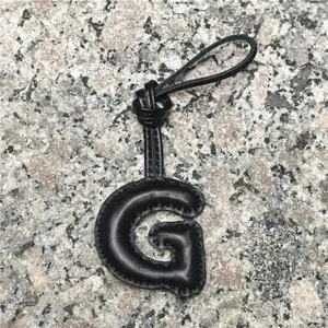 Detailed view of the black leather letter G bag charm featuring soft puff texture and loop.