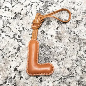Detail view of light brown leather letter L bag charm pendant, elegant initial accessory.