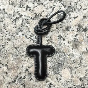 Black leather letter T bag charm detail showcasing fine stitching and smooth texture.