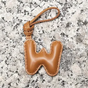 Close-up detail of a light brown leather puffy letter W bag charm with contrast stitching.