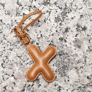 Close-up detail of the light brown leather letter X charm, showing fine stitching and texture.