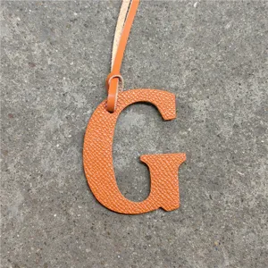 Detailed view of the orange leather letter G bag charm with dual straps and fine texture.