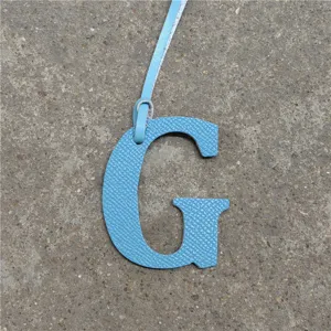 Close-up detail of light blue leather letter G bag charm with hanging strap, stylish accessory.