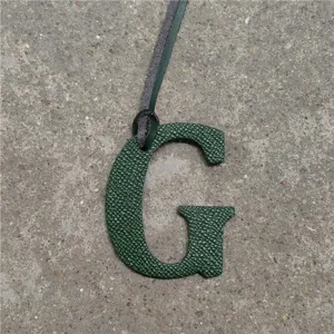 Green leather letter G bag charm detail, textured leather monogram pendant with hanging cord.