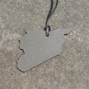 Leather map pendant keychain detail view showing textured grey surface and hanging cord.