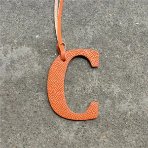 Orange leather letter C bag charm, detailed closeup showing fine textured leather finish and strap.