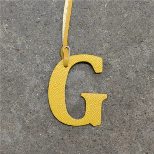 Yellow leather letter G handbag charm close-up, stylish initial pendant accessory.