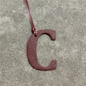 Close-up detail of a burgundy leather letter C bag charm pendant with a hanging strap.
