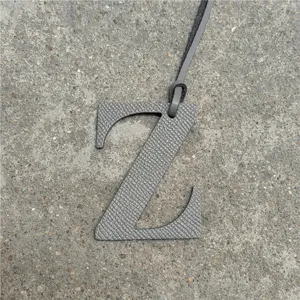 Detalle de dije de bolsa letra Z de cuero gris, elegante accesorio con correa colgante.