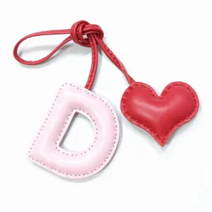 Closeup detail of a handmade pink leather letter D and red heart bag charm pendant.