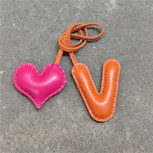 Detalle de dije de cuero hecho a mano con corazón rosa y colgante V naranja.
