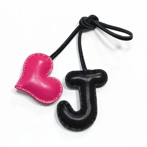 Dettaglio del ciondolo in pelle fatta a mano con lettera J e cuore rosa per borse e auto.