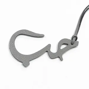 Gros plan sur le charm de sac en cuir gris avec lettre arabe, montrant les détails et la lanière.