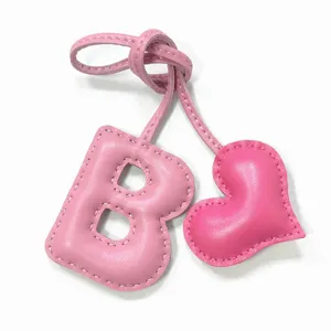 Detalle de dije de bolso de cuero rosa hecho a mano letra B y corazon, accesorio mono.