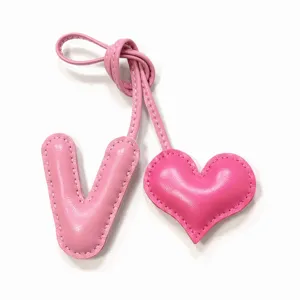 Primer plano del dije de bolso de cuero rosa hecho a mano con letra V y corazón y costuras.