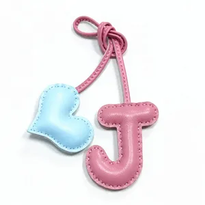 Vista di dettaglio del ciondolo borsa lettera J in pelle rosa e cuore azzurro con cuciture.
