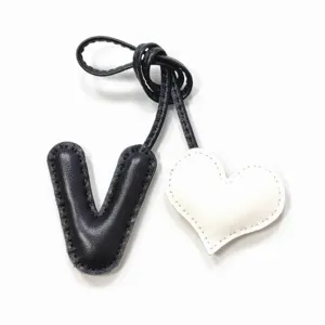 Colgante artesanal de cuero negro con letra V y corazón blanco para bolsos y coche.