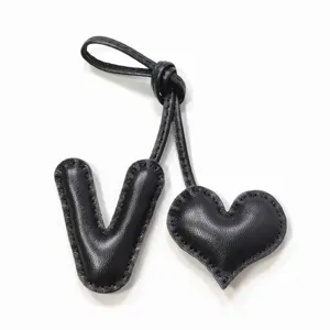 Vista detallada del dije de bolso en cuero negro con letra V y corazón cosido a mano.