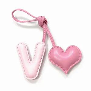 Detalle de dije de bolso letra V y corazón de cuero rosa, llavero hecho a mano.